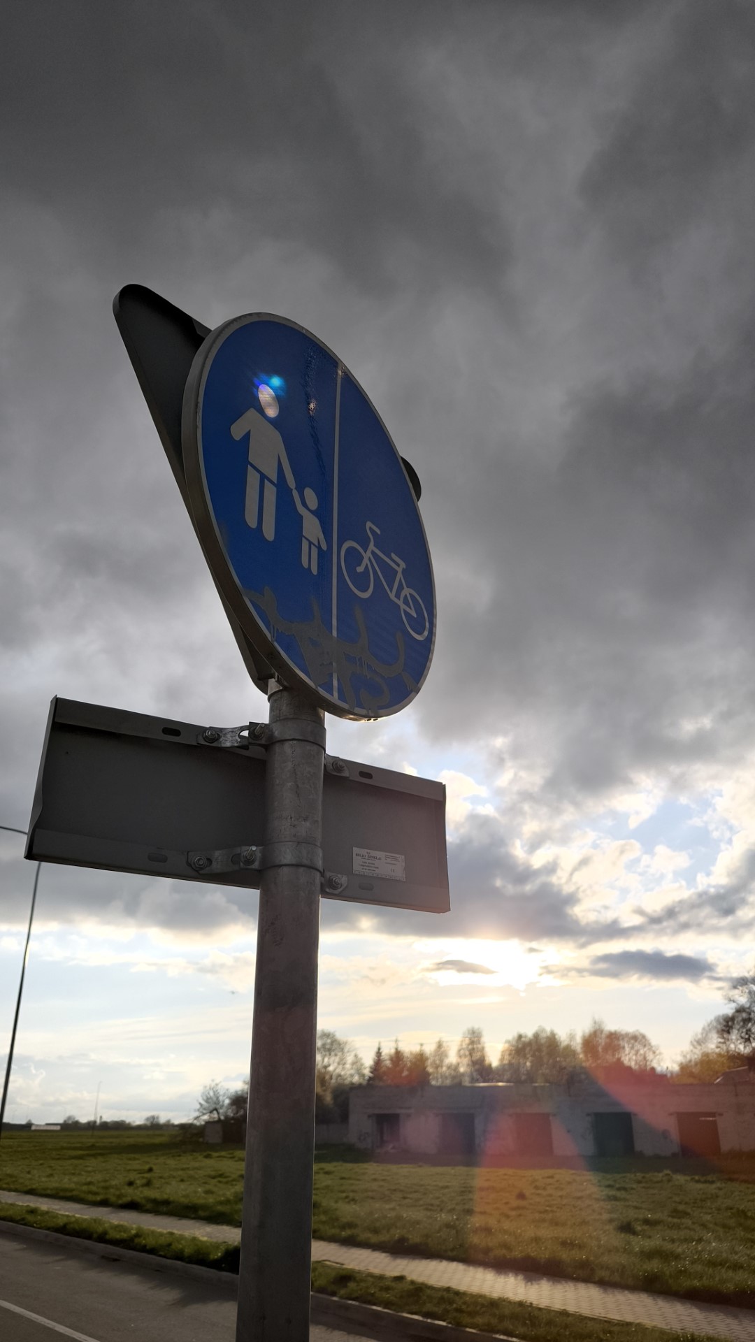 A photo of a street sign. The sun is setting in the background and is causing a rainbow to form on the street sign through reflections.